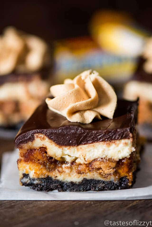 Reese's Butterfinger Cheesecake Bars are our copycat version of The Cheesecake Factory's Adam's Peanut Butter Cup Fudge Ripple Cheesecake. Creamy cheesecake stuffed with two kinds of candy bars, caramel, and topped with chocolate ganache and peanut butter frosting.
