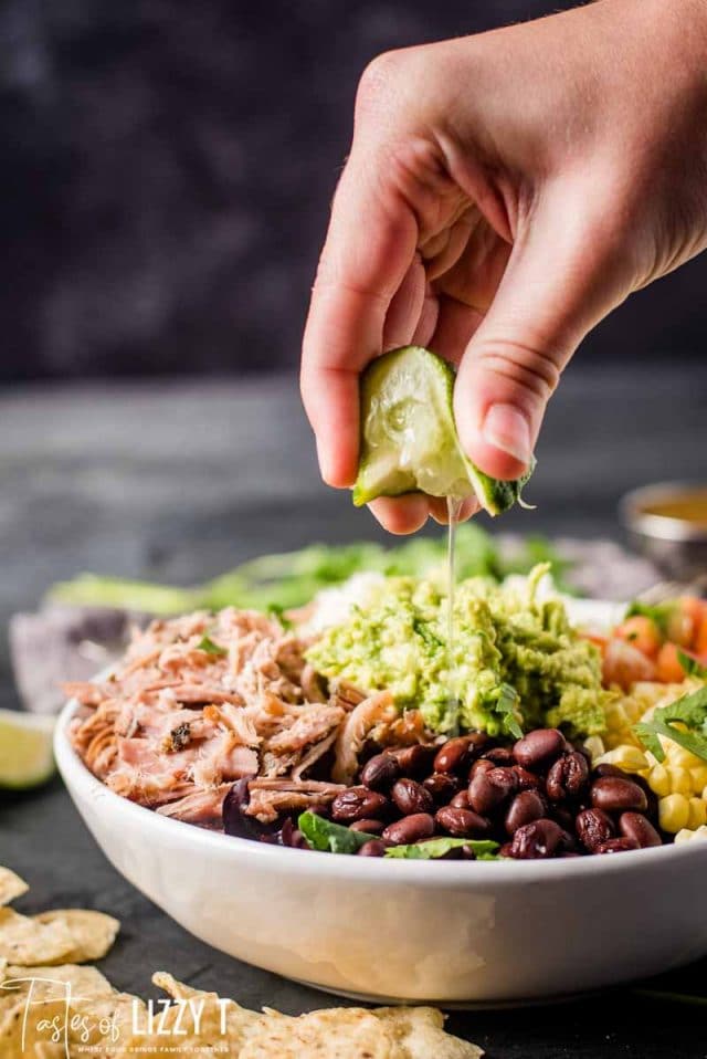 A person holding a lime and sprinkling over salad