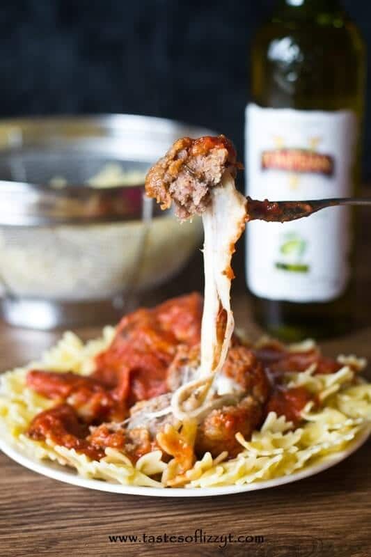 dinner fork holding a cheese stuffed meatball. A large amount of mozzarella cheese is oozing from the meatball