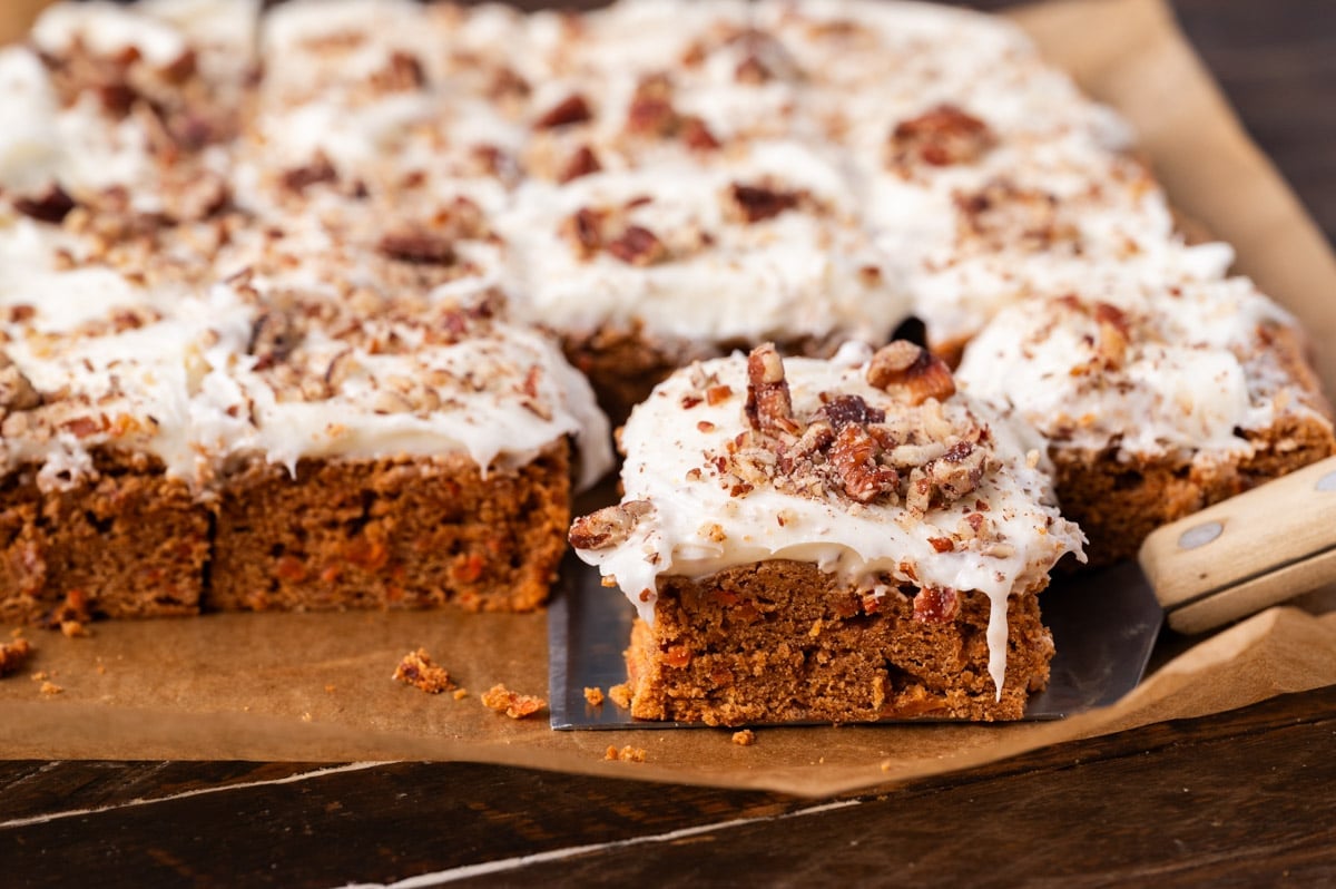 carrot cake bars sitting on a table, one on a spatula