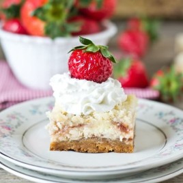 Strawberry Shortcake Cheesecake Bars on a plate with whipped cream and strawberry