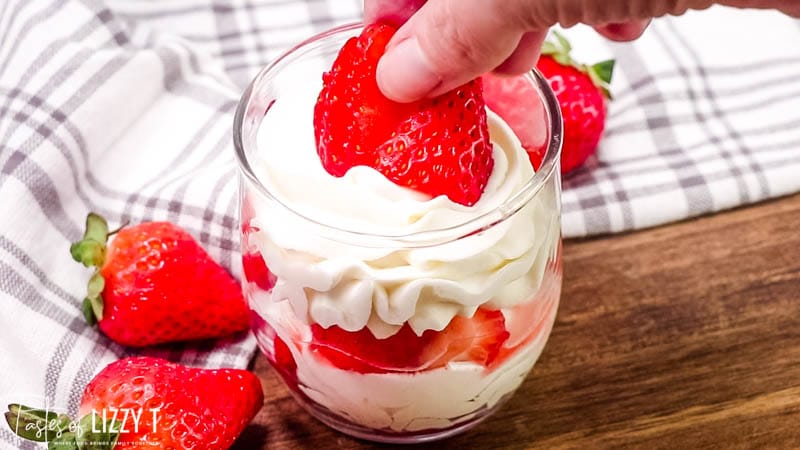 A close up of a person placing strawberries in a parfait