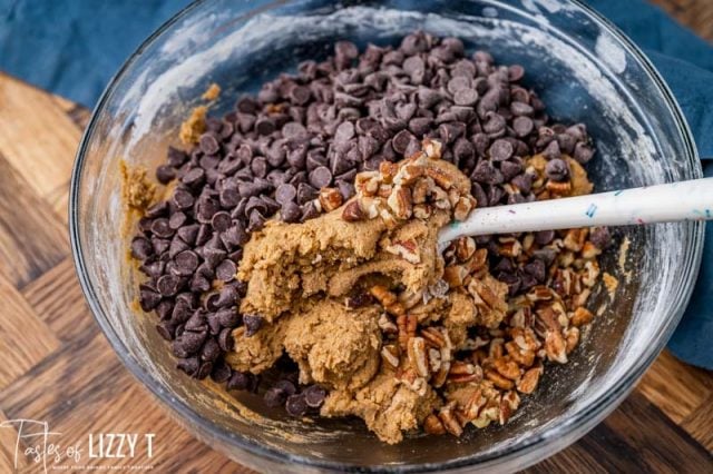 chocolate chips and pecans over cookie batter in a bowl