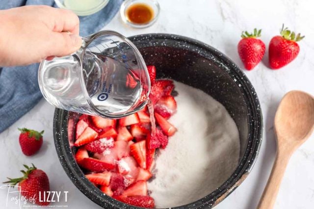 pouring water in saucepan with strawberries and sugar