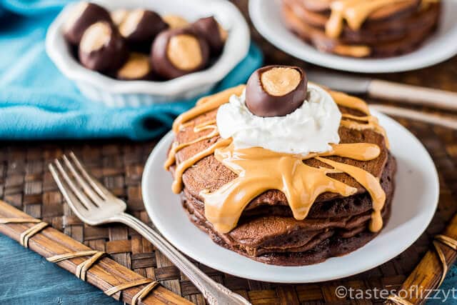 Peanut butter buckeye candy filling is cooked inside these fluffy chocolate peanut butter pancakes. Drizzle with peanut butter, whipped cream and a buckeye.