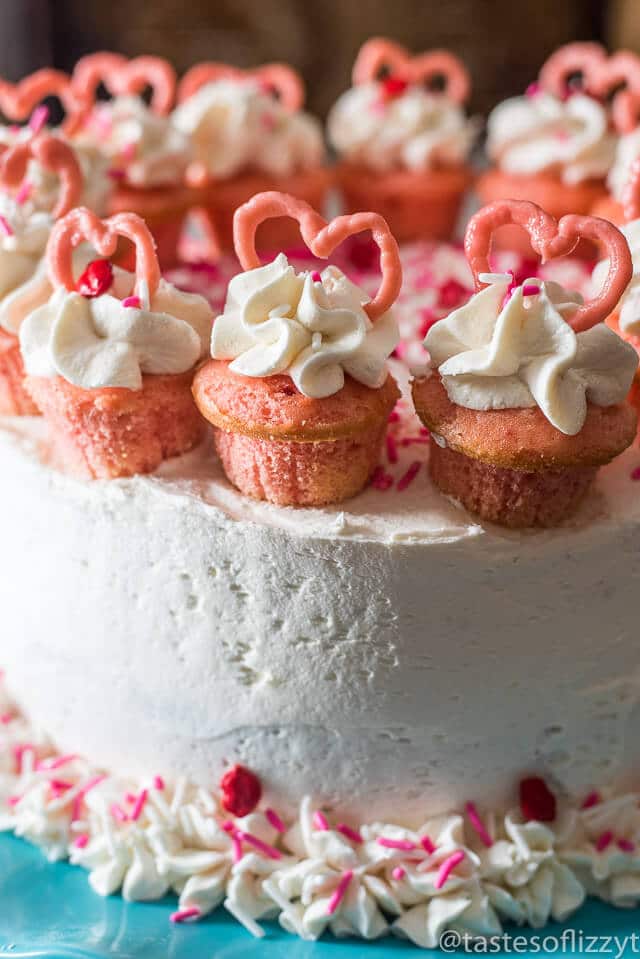 Serve your loved ones this easy-to-decorate strawberry valentine cake. Vanilla buttercream frosted strawberry cake with mini cupcakes, pink candy hearts and sprinkles.