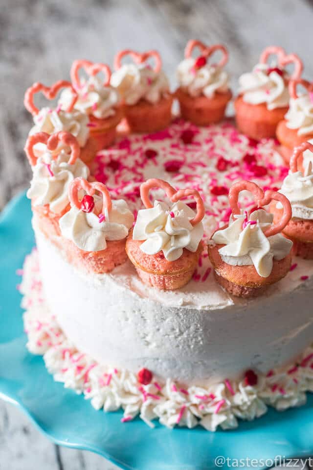 Serve your loved ones this easy-to-decorate strawberry valentine cake. Vanilla buttercream frosted strawberry cake with mini cupcakes, pink candy hearts and sprinkles.