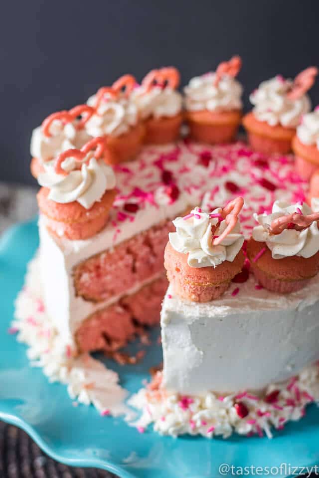 Serve your loved ones this easy-to-decorate strawberry valentine cake. Vanilla buttercream frosted strawberry cake with mini cupcakes, pink candy hearts and sprinkles.