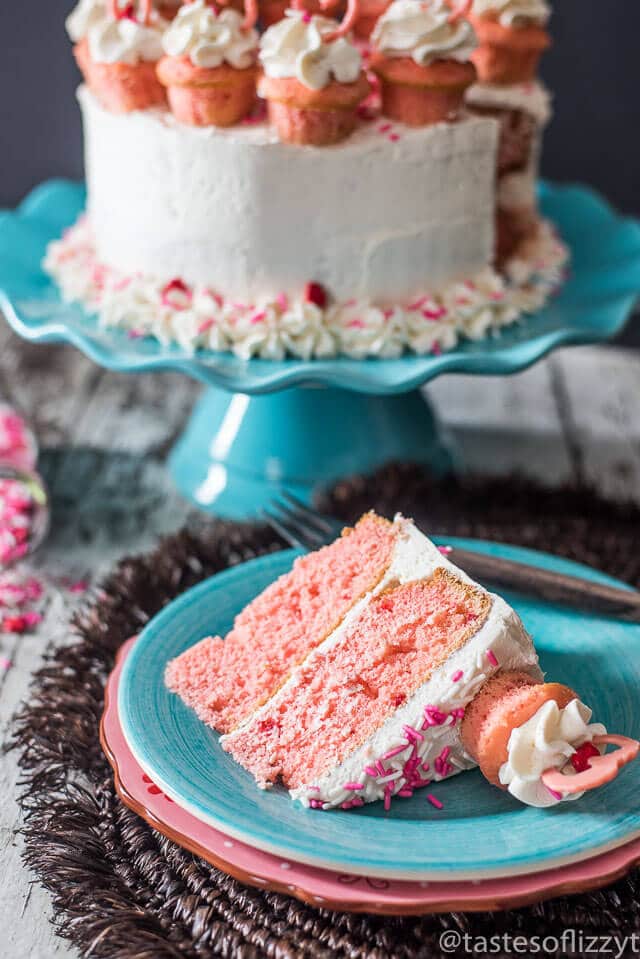 Serve your loved ones this easy-to-decorate strawberry valentine cake. Vanilla buttercream frosted strawberry cake with mini cupcakes, pink candy hearts and sprinkles.