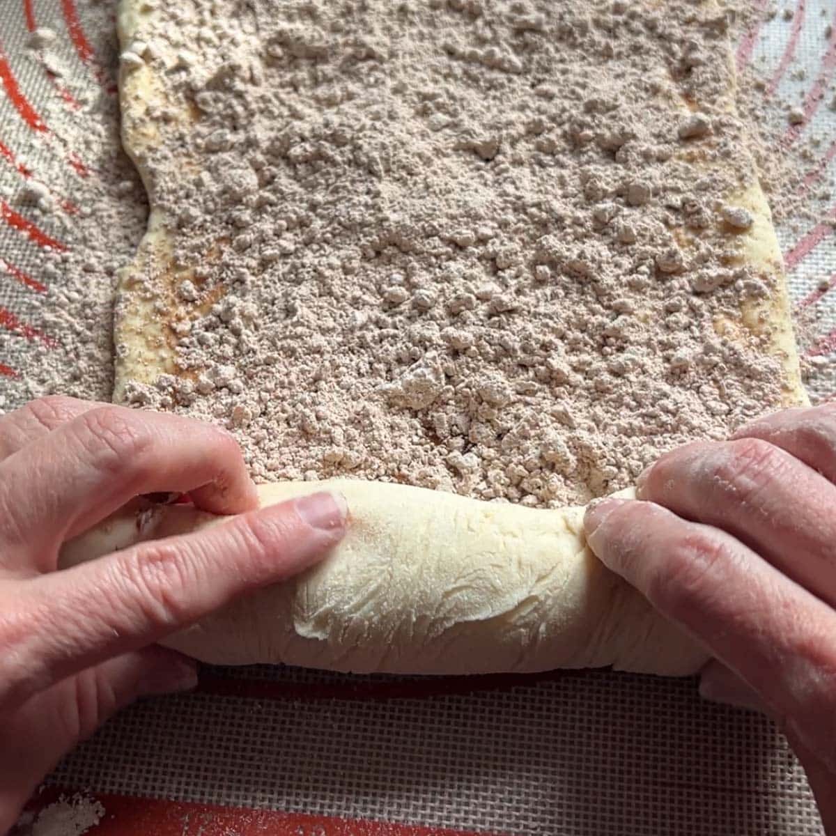 hands rolling up dough for cinnamon bread