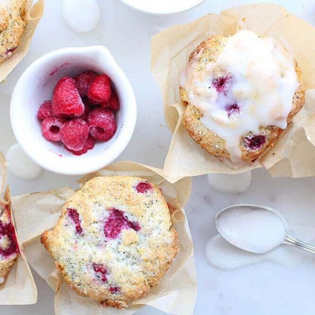 two lemon poppyseed raspberry muffins with a bowl of raspberries