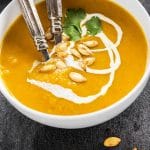 bowl of pumpkin apple carrot soup garnished with pepitas