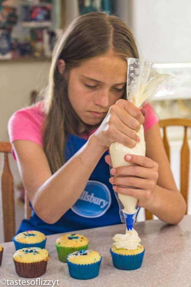 A woman sitting at a table decorating a cupcake