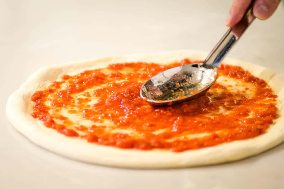 spreading sauce on pizza crust