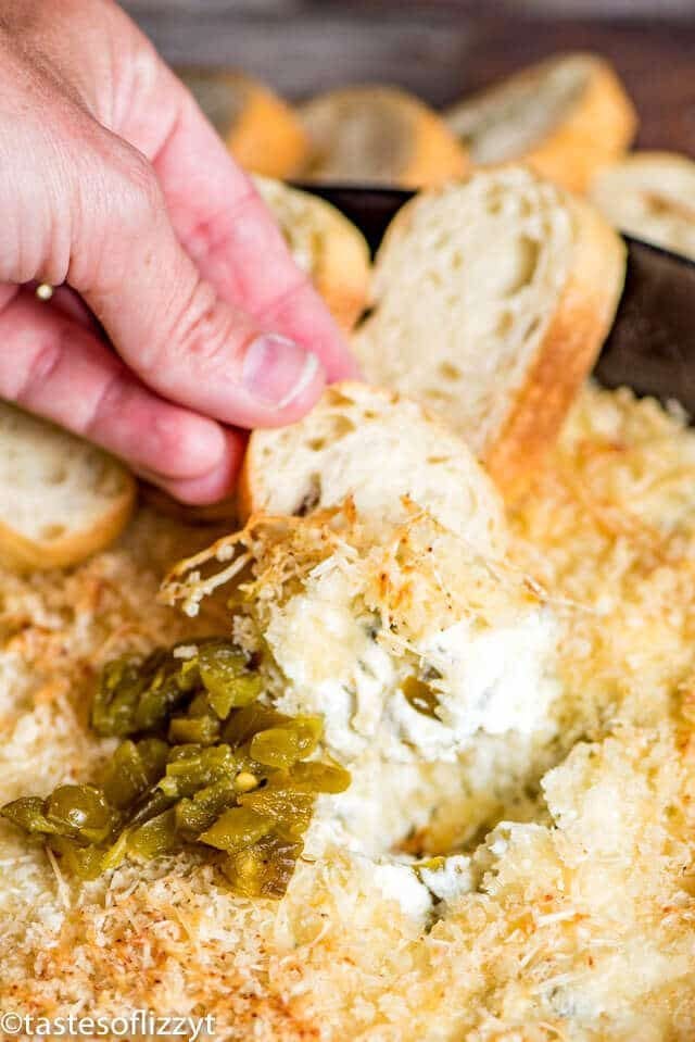 A close up of hand dipping bread in jalapeno popper dip