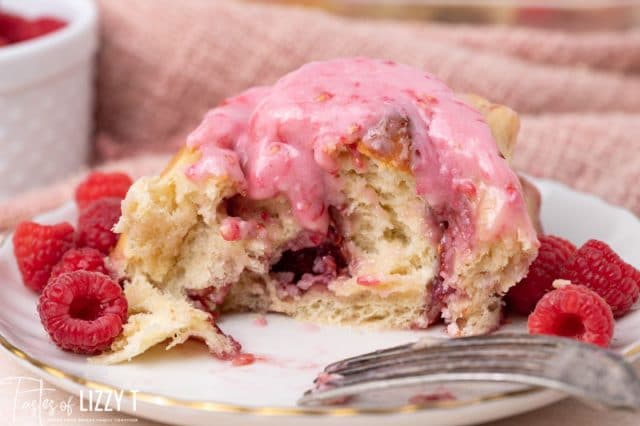 half of a sweet roll on a plate with a fork