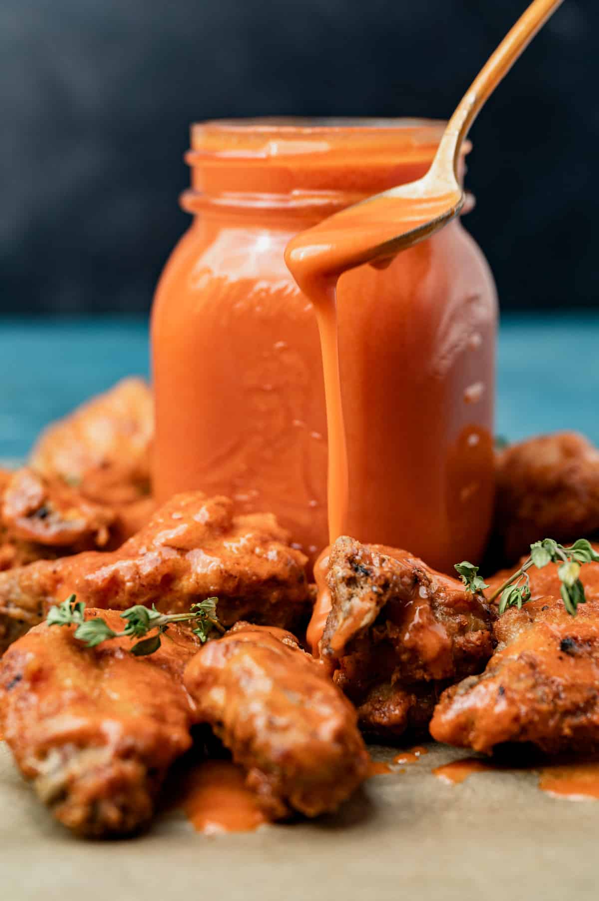 spoon drizzling buffalo sauce over chicken wings