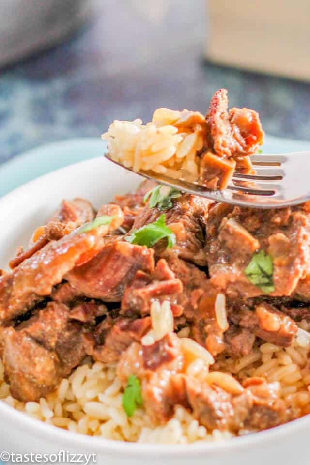 A close up of a plate of food, with Beef tips and rice on a fork