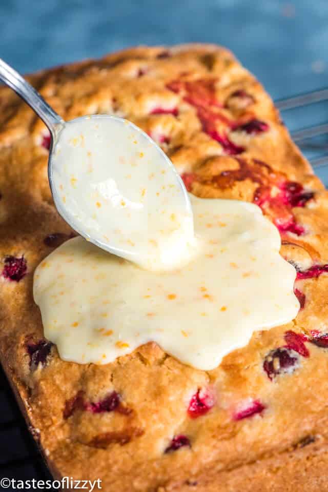 spooning orange glaze on a loaf of cranberry bread