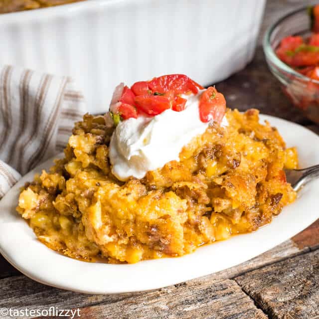 A bowl of food on a plate, with Taco Casserole and sour cream