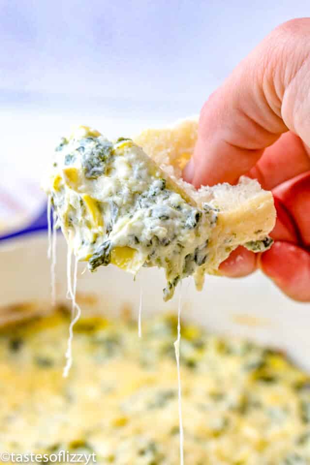 a hand holding bread with spinach dip
