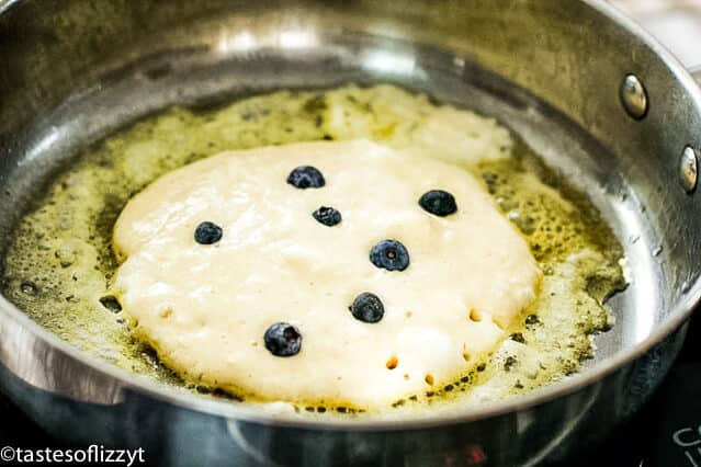 blueberry pancakes cooking in a skillet