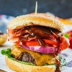 A close up of a sandwich sitting on top of a paper plate, with Bacon and Cheeseburger