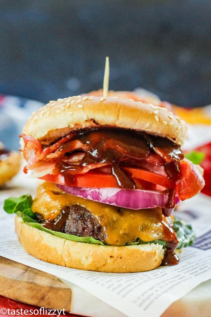 A close up of a sandwich sitting on top of a paper plate, with Bacon and Cheeseburger