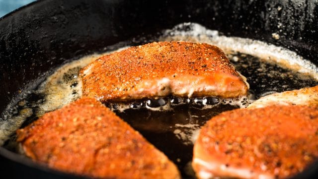 A close up of a piece of salmon frying in skillet