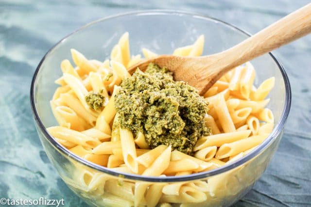 mixing penne and pesto in a bowl