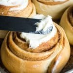Spreading cream cheese frosting on a cinnamon roll