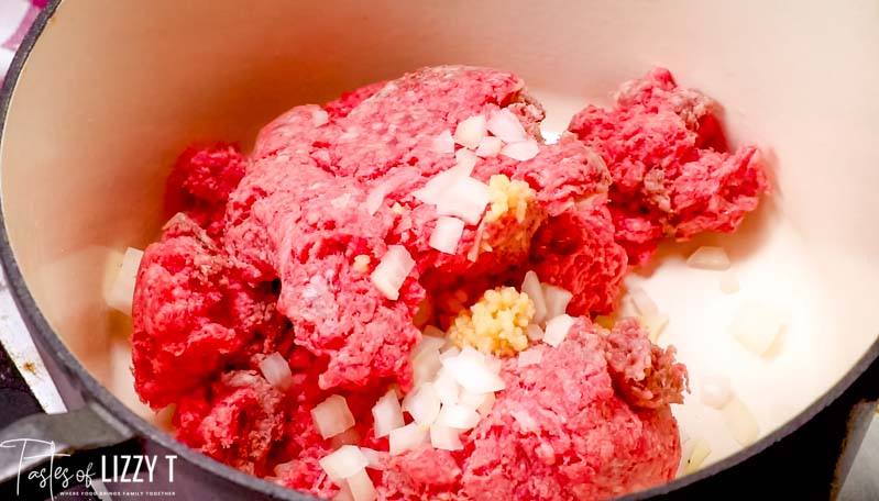 A close up of uncooked beef and onion and garlic in a skillet
