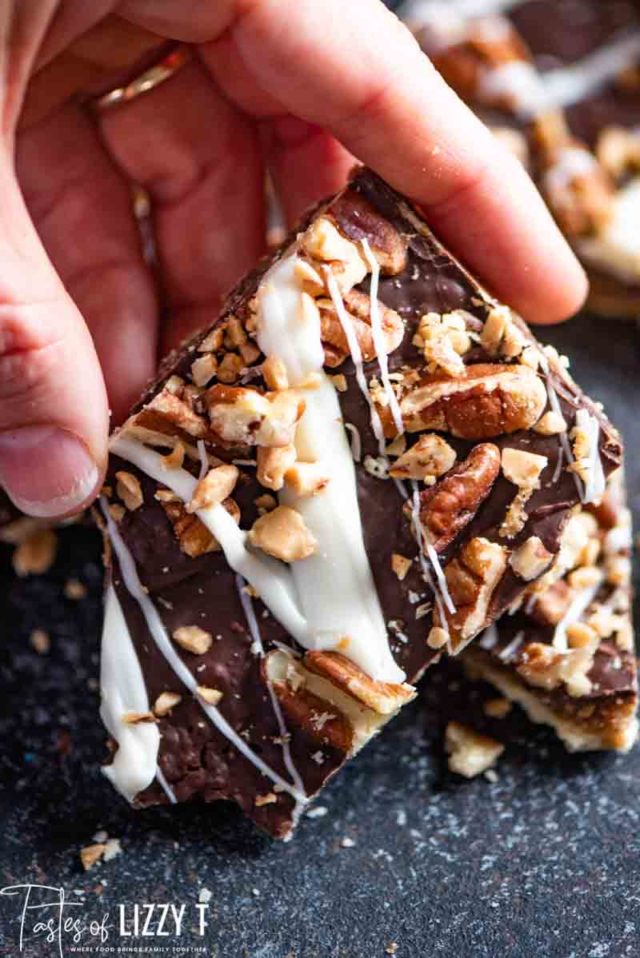 A close up of a person holding a piece of saltine toffee