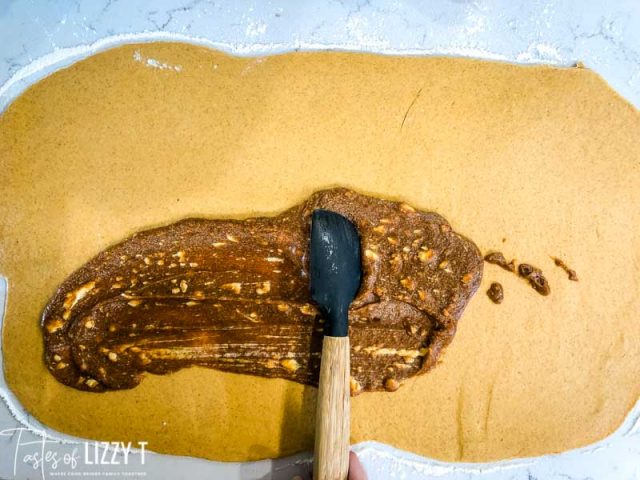 spreading cinnamon roll filling on pumpkin dough