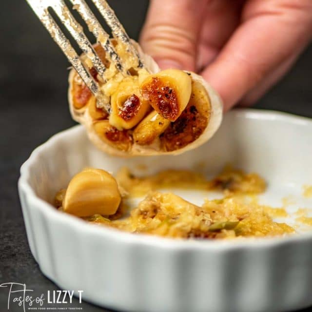 A person holding roasted garlic and a fork