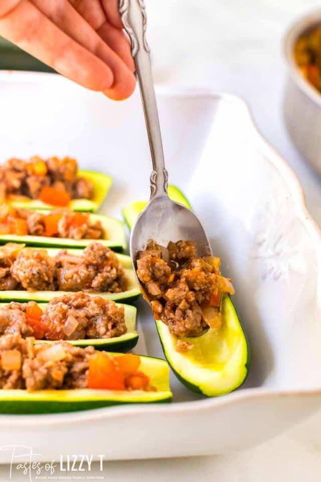spoon filling zucchini boats with browned sausage