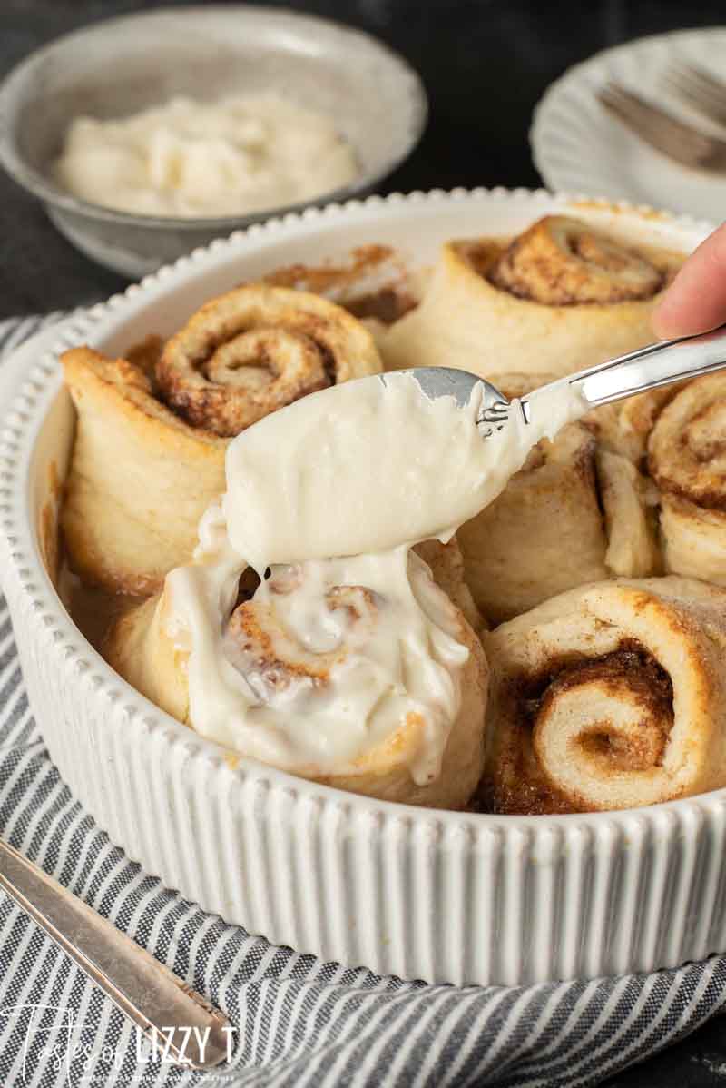 bisquick cinnamon rolls with powdered sugar glaze being spread on top