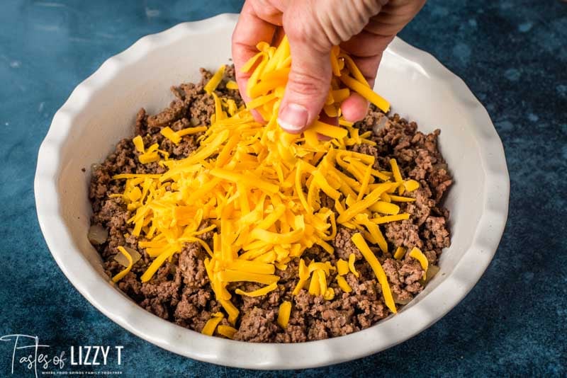 sprinkling cheddar cheese on ground beef in baking dish