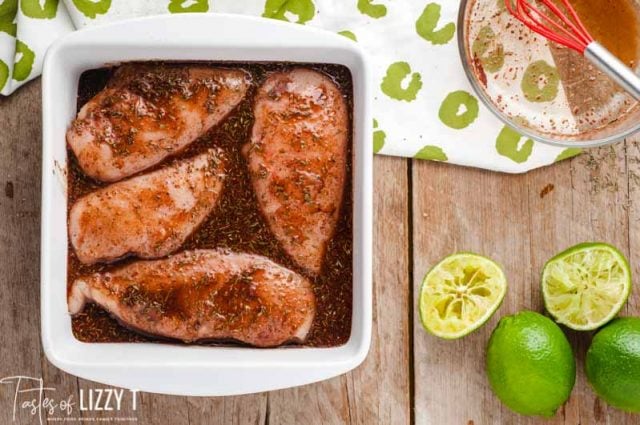 chicken marinating in a dish with limes