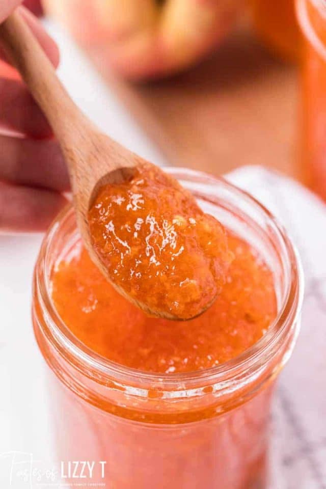 peach freezer jam in a glass jar with a wooden spoon