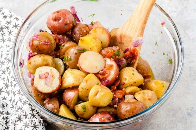 warm potato salad in mixing bowl with wooden spoon