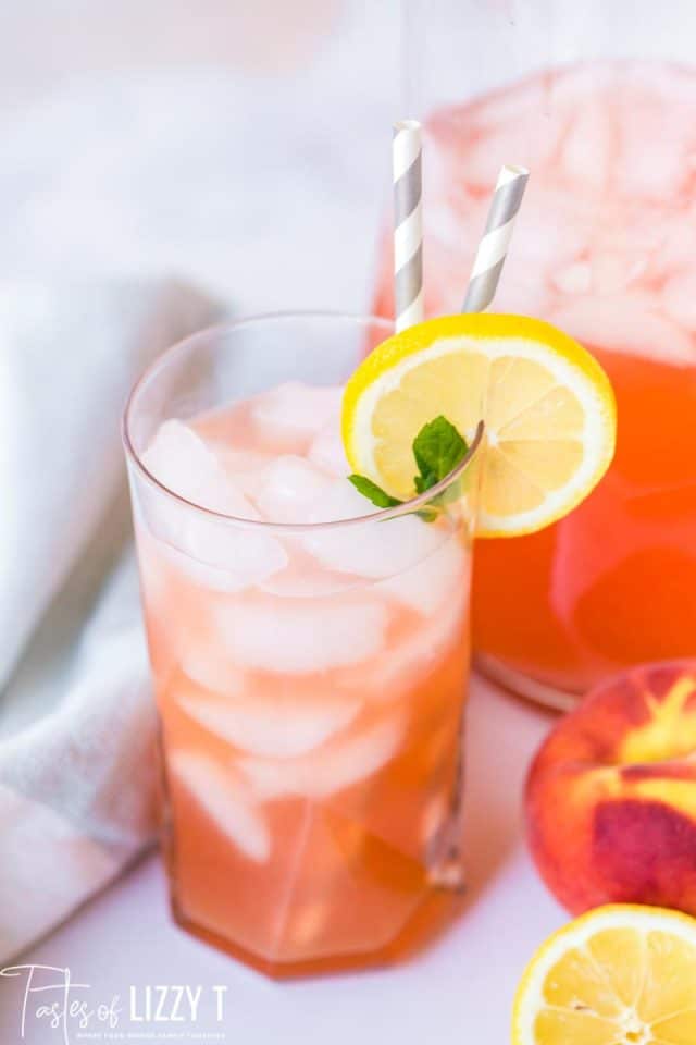 a glass of homemade peach lemonade with two straws and a slice of lemon