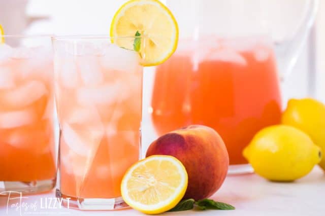 two glasses of peach lemonade with fresh peaches and lemons