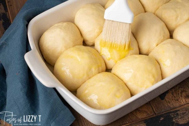 pastry brush brushing egg wash on top of unbaked sourdough rolls