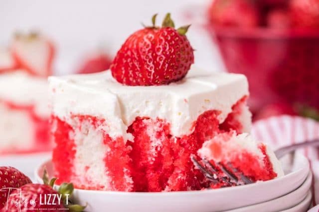 piece of strawberry jello poke cake on a plate with a fork with a bite on it
