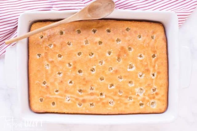 white cake with holes poked in the top by end of wooden spoon