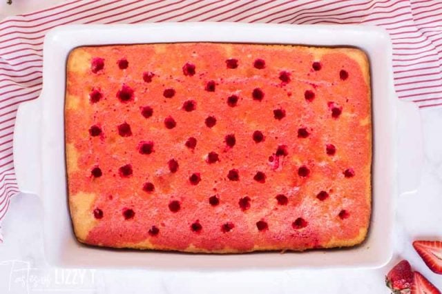 white cake with holes poked in top and strawberry jello poured over it