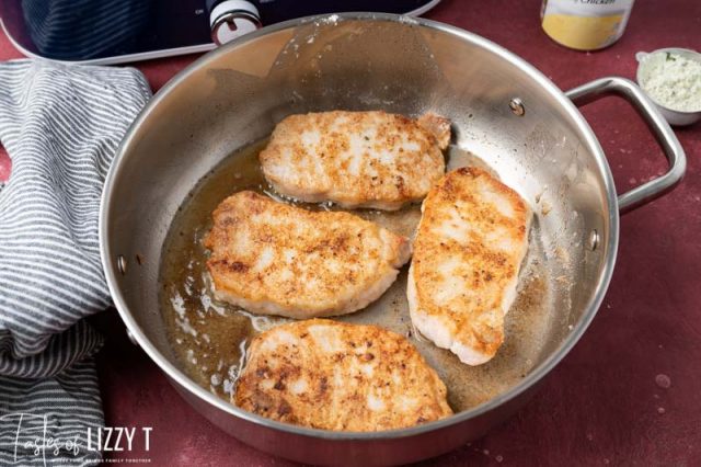 4 pork chops searing in a skillet