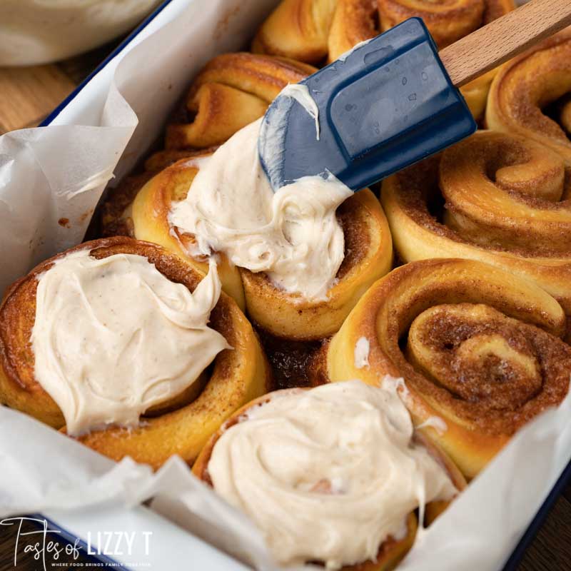 spreading frosting on eggnog cinnamon rolls