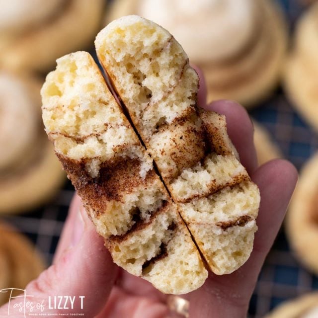 a hand holding a cinnamon roll cookie broken in half